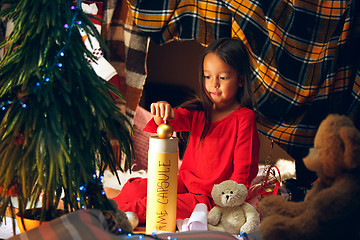 Image showing Merry Christmas and Happy Holidays. Cute little child girl writes the letter to Santa Claus near Christmas tree