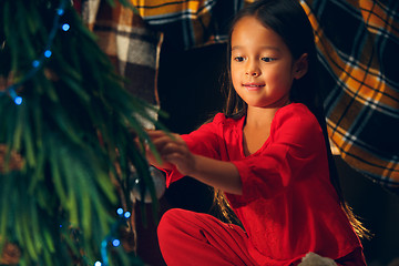 Image showing christmas, holidays and childhood concept - happy girl in red clothes decorating natural fir tree