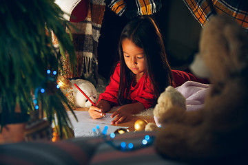 Image showing Merry Christmas and Happy Holidays. Cute little child girl writes the letter to Santa Claus near Christmas tree