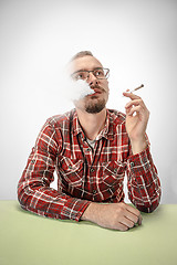 Image showing Handsome hipster man smoking cigarette at home. Man looking upwards and enjoying spending free time.