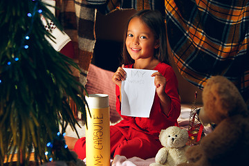 Image showing Merry Christmas and Happy Holidays. Cute little child girl writes the letter to Santa Claus near Christmas tree