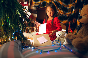 Image showing Merry Christmas and Happy Holidays. Cute little child girl writes the letter to Santa Claus near Christmas tree