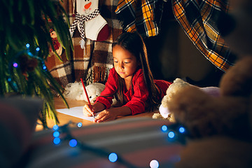 Image showing Merry Christmas and Happy Holidays. Cute little child girl writes the letter to Santa Claus near Christmas tree