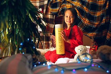 Image showing Merry Christmas and Happy Holidays. Cute little child girl writes the letter to Santa Claus near Christmas tree