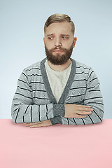 Image showing Serious business man sitting at a table on a blue background