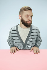 Image showing Serious business man sitting at a table on a blue background