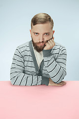 Image showing Serious business man sitting at a table on a blue background