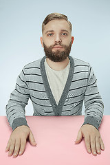 Image showing Serious business man sitting at a table on a blue background