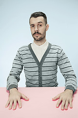 Image showing Serious business man sitting at a table on a blue background