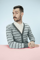 Image showing Serious business man sitting at a table on a blue background