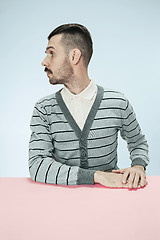 Image showing Serious business man sitting at a table on a blue background