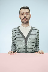 Image showing Serious business man sitting at a table on a blue background