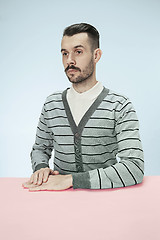 Image showing Serious business man sitting at a table on a blue background