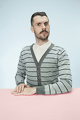 Image showing Serious business man sitting at a table on a blue background