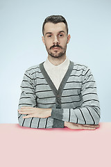 Image showing Serious business man sitting at a table on a blue background