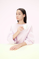 Image showing Beautiful lonely woman sitting at studio and looking sad holding the cup of coffee in hand. Closeup toned portrait