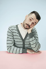 Image showing Serious business man sitting at a table on a blue background