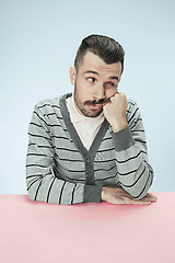 Image showing Serious business man sitting at a table on a blue background