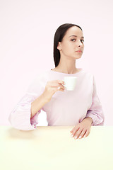 Image showing Beautiful lonely woman sitting at studio and looking sad holding the cup of coffee in hand. Closeup toned portrait