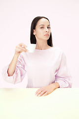 Image showing Beautiful lonely woman sitting at studio and looking sad holding the cup of coffee in hand. Closeup toned portrait