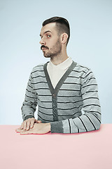 Image showing Serious business man sitting at a table on a blue background