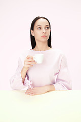 Image showing Beautiful lonely woman sitting at studio and looking sad holding the cup of coffee in hand. Closeup toned portrait