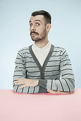 Image showing Surprised business man sitting at a table on a blue background