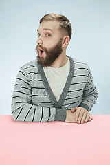 Image showing Surprised business man sitting at a table on a blue background