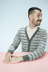 Image showing The happy smiling businessman sitting at a table on a blue background