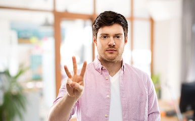 Image showing young man showing three fingers over office