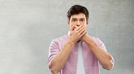 Image showing shocked young man covering his mouth by hands