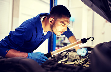 Image showing mechanic man with lamp repairing car at workshop