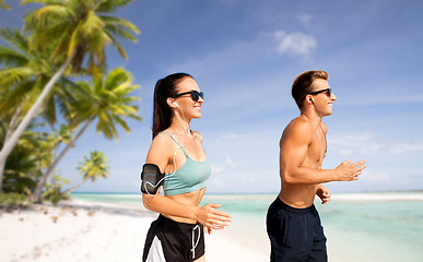 Image showing couple with phones and arm bands running on beach