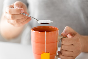 Image showing close up of woman adding sugar to cup of tea