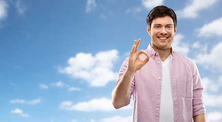 Image showing smiling young man showing ok hand sign over sky