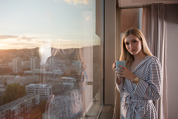 Image showing young woman enjoying evening coffee by the window