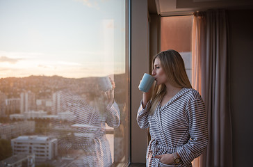 Image showing young woman enjoying evening coffee by the window