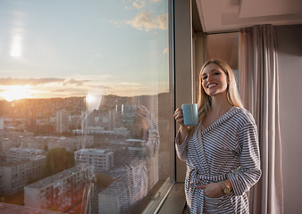 Image showing young woman enjoying evening coffee by the window