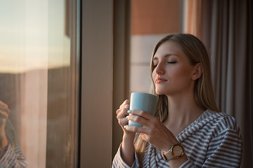 Image showing young woman enjoying evening coffee by the window