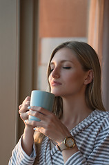 Image showing young woman enjoying evening coffee by the window