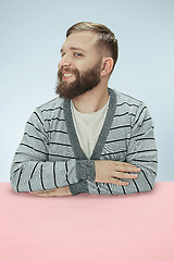 Image showing The happy smiling businessman sitting at a table on a blue background