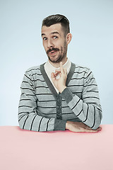 Image showing The happy smiling businessman sitting at a table on a blue background