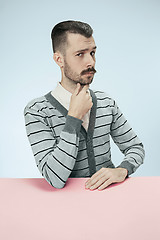 Image showing Serious business man sitting at a table on a blue background