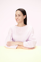 Image showing The happy and smiling business woman sitting at a table on a pink background