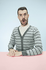 Image showing Surprised business man sitting at a table on a blue background