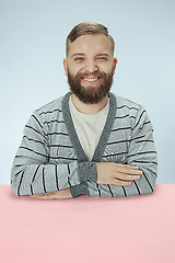 Image showing The happy smiling businessman sitting at a table on a blue background