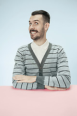 Image showing The happy smiling businessman sitting at a table on a blue background