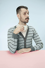 Image showing lonely man sitting at studio and looking sad holding the cup of coffee in hand. Closeup toned portrait