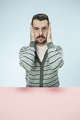 Image showing portrait of stressed man sitting at table with closed and covering her ears with hands.