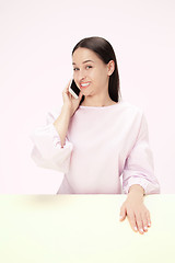 Image showing The happy business woman sitting with mobile phone against pink background.